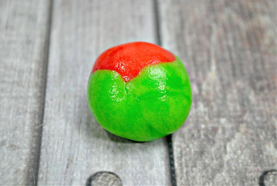 red and green dough mixed together and shaped into a ball on a wooden background