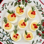 eight holiday deviled eggs on a plate with holly printed on it