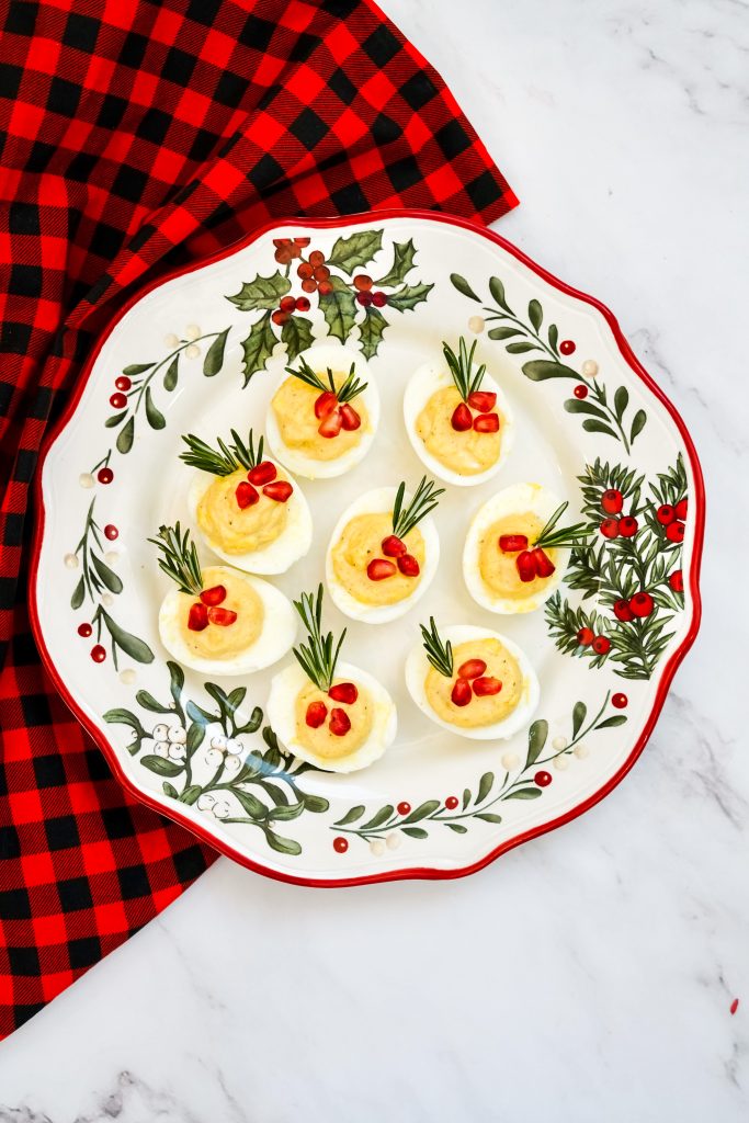 eight holiday deviled eggs on a plate with a holly designs