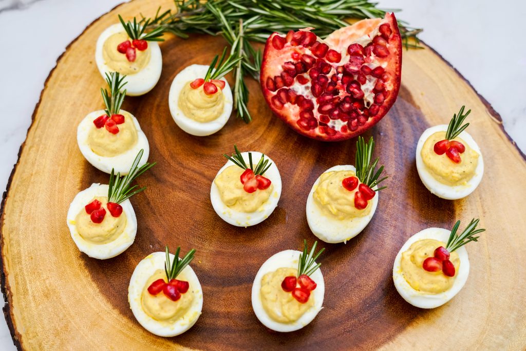garnished deviled eggs on a wooden board with a pomegranate