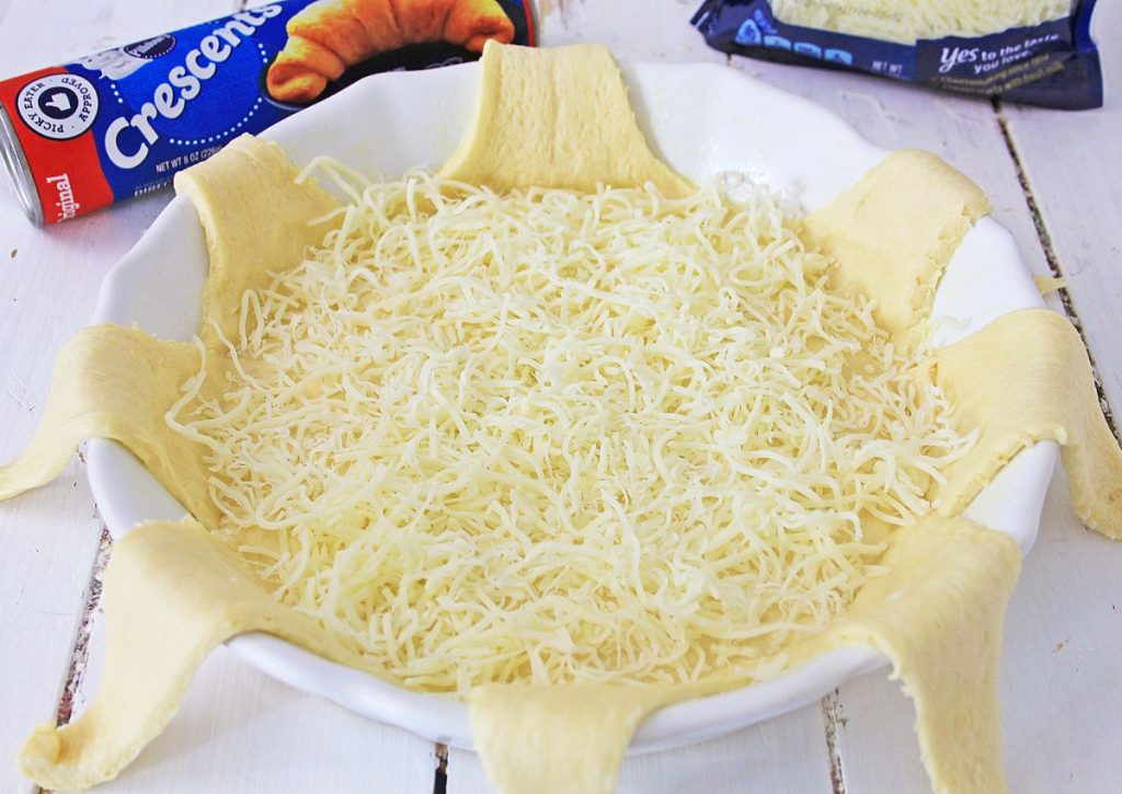 shredded cheese sprinkled on top of crescent rolls in a pie plate 