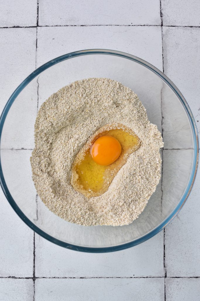 egg being added to matzo flour in a glass bowl. 