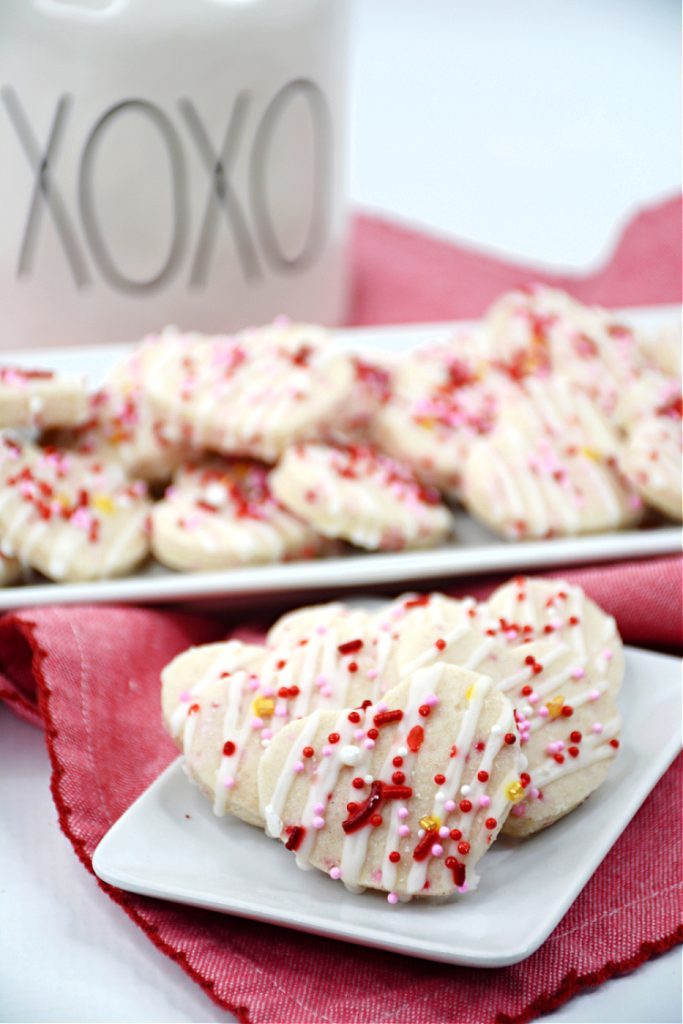 Plateful of heart-shaped mini Valentine shortbread cookies in front of serving platter with more Valentine cookies
