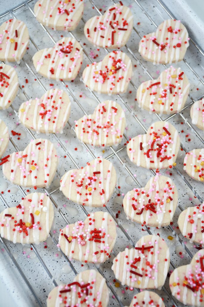 sprinkles being added to the top of shortbread cookies on a wire rack.