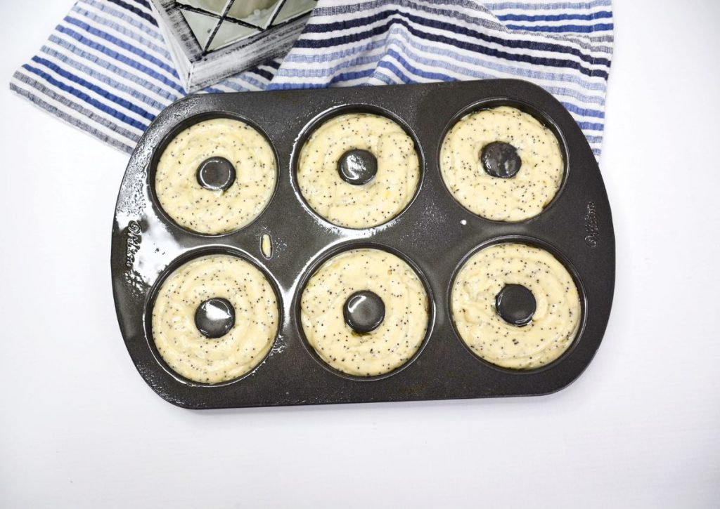 poppy seed donut batter being piped into a donut pan.