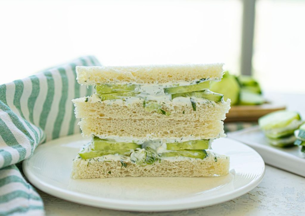 Two halves of cucumber and dill sandwiches stacked on a plate.