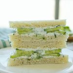 Two halves of cucumber and dill sandwiches stacked on a plate.
