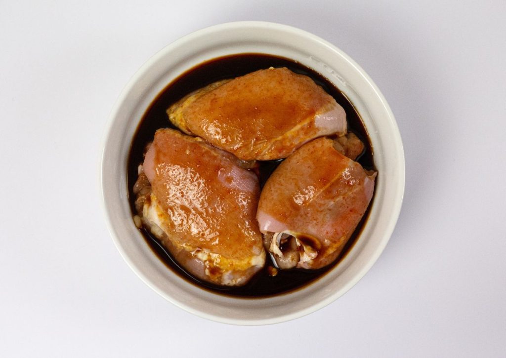 Meat being marinated in a white bowl.