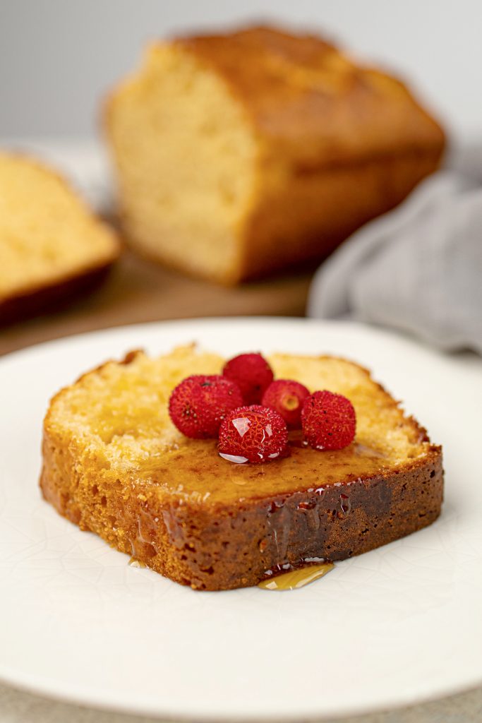 A slice of vanilla protein cake topped with berries on a white plate.