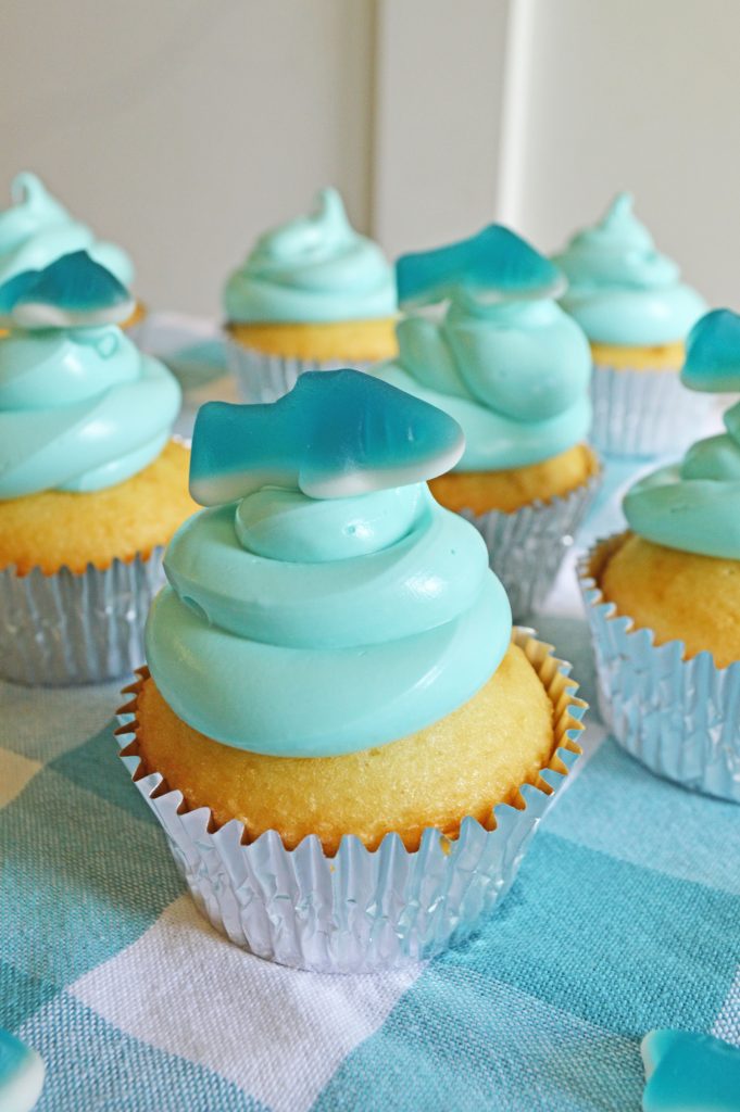 vanilla cupcakes topped with blue cream cheese frosting and a gummy shark