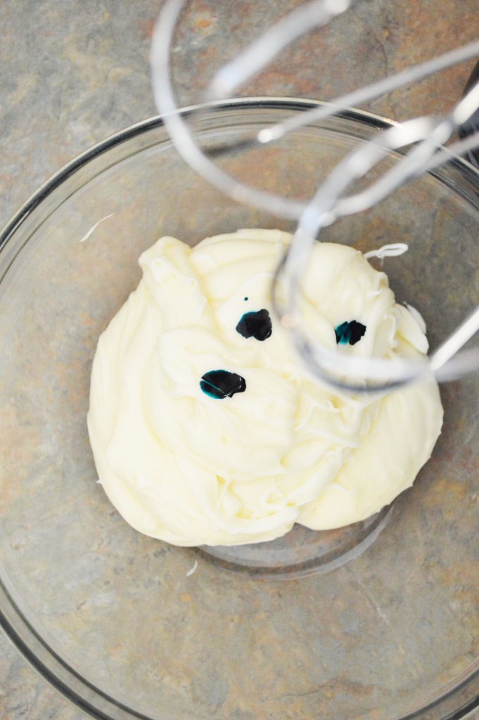 adding drops of blue food coloring to the cream cheese frosting