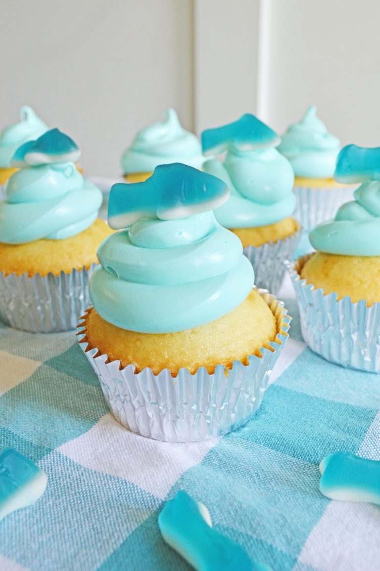 Shark cupcakes with blue frosting sitting on the table.