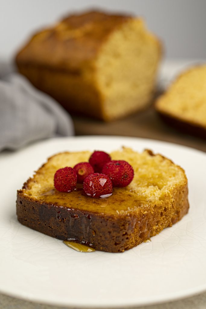 Piece of protein cake on a white plate with some fruit on top.